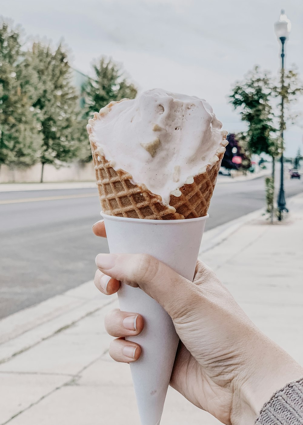 a person holding an ice cream cone on a sidewalk