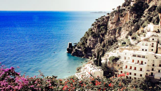 A sunlit coastal villa overlooking the turquoise sea with vibrant bougainvillea in full bloom.