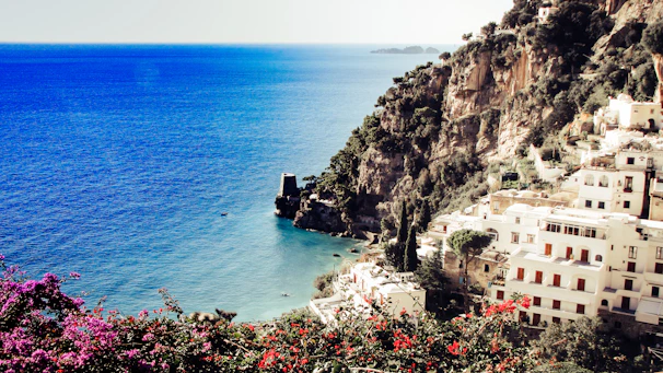 A sunlit coastal villa overlooking the turquoise sea with vibrant bougainvillea in full bloom.