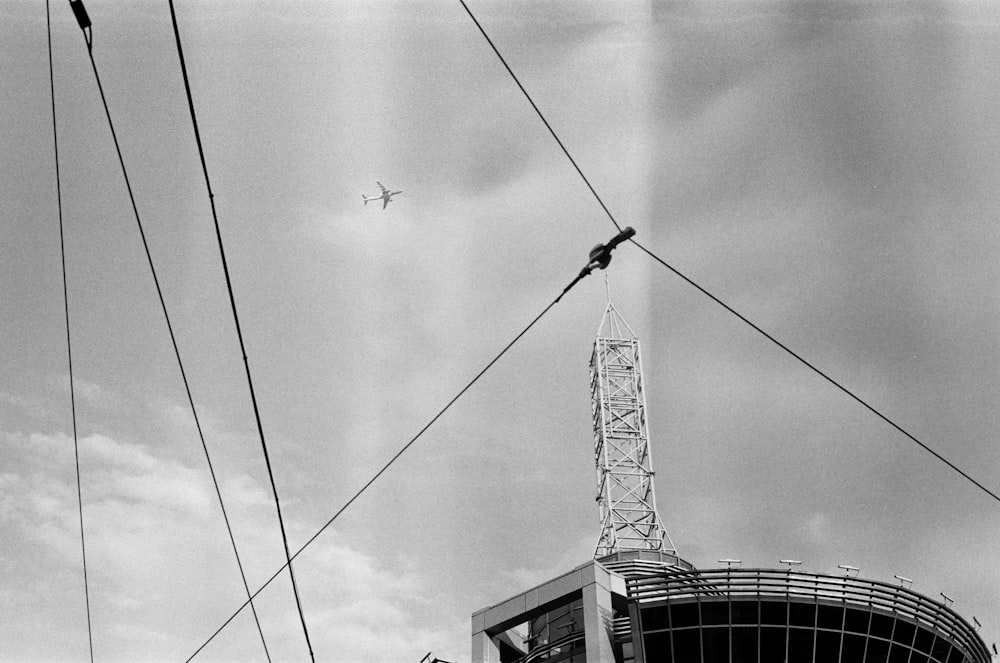 grayscale photography of airplane flying above building with tower