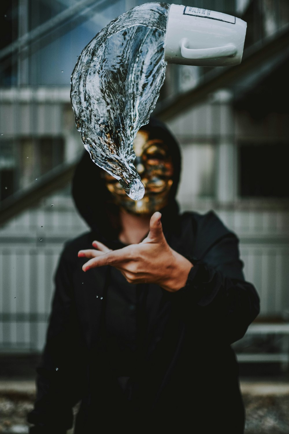 man wearing gold-colored mask and black hooded jacket tossed white ceramic mug with water