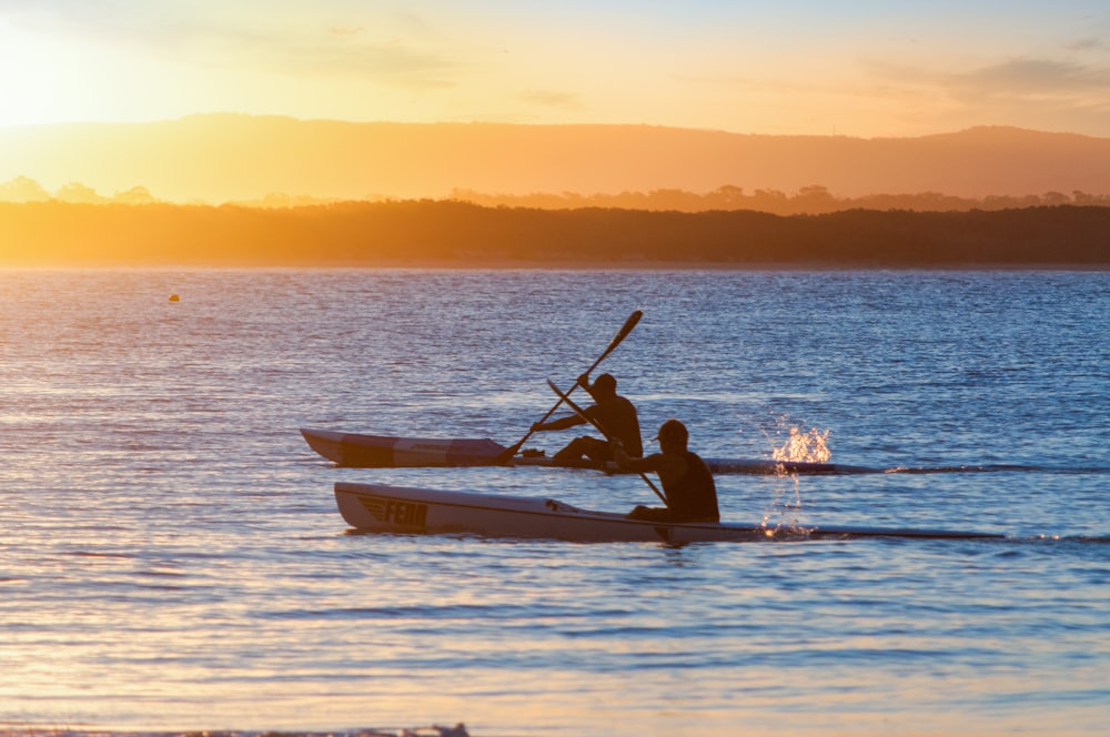 two men rowing canoes during golden hour