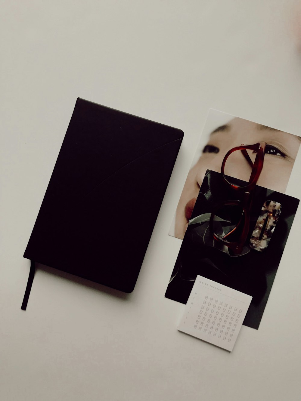 Schwarzes Buch neben braunen Brillen und Fotos