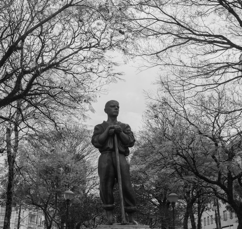 grayscale photography of man standing statue near trees