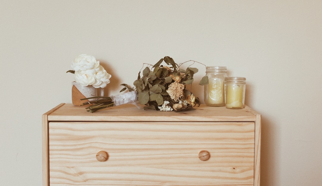 Light wooden dresser top styled with dried flower bouquets and glass jar candles against a neutral wall