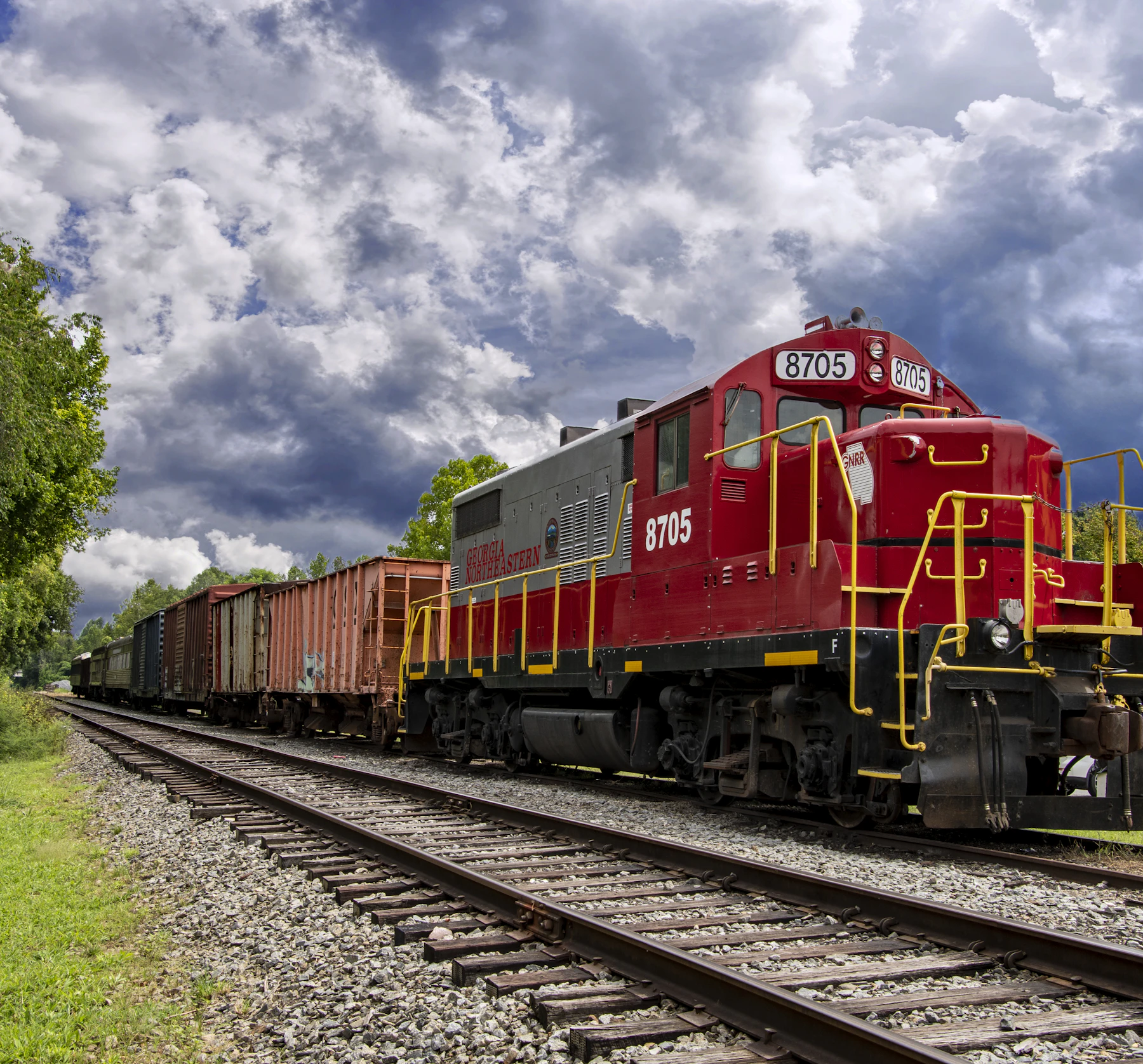 A red diesel locomotive numbered 8705 with yellow handrails leading boxcars under a cloudy sky