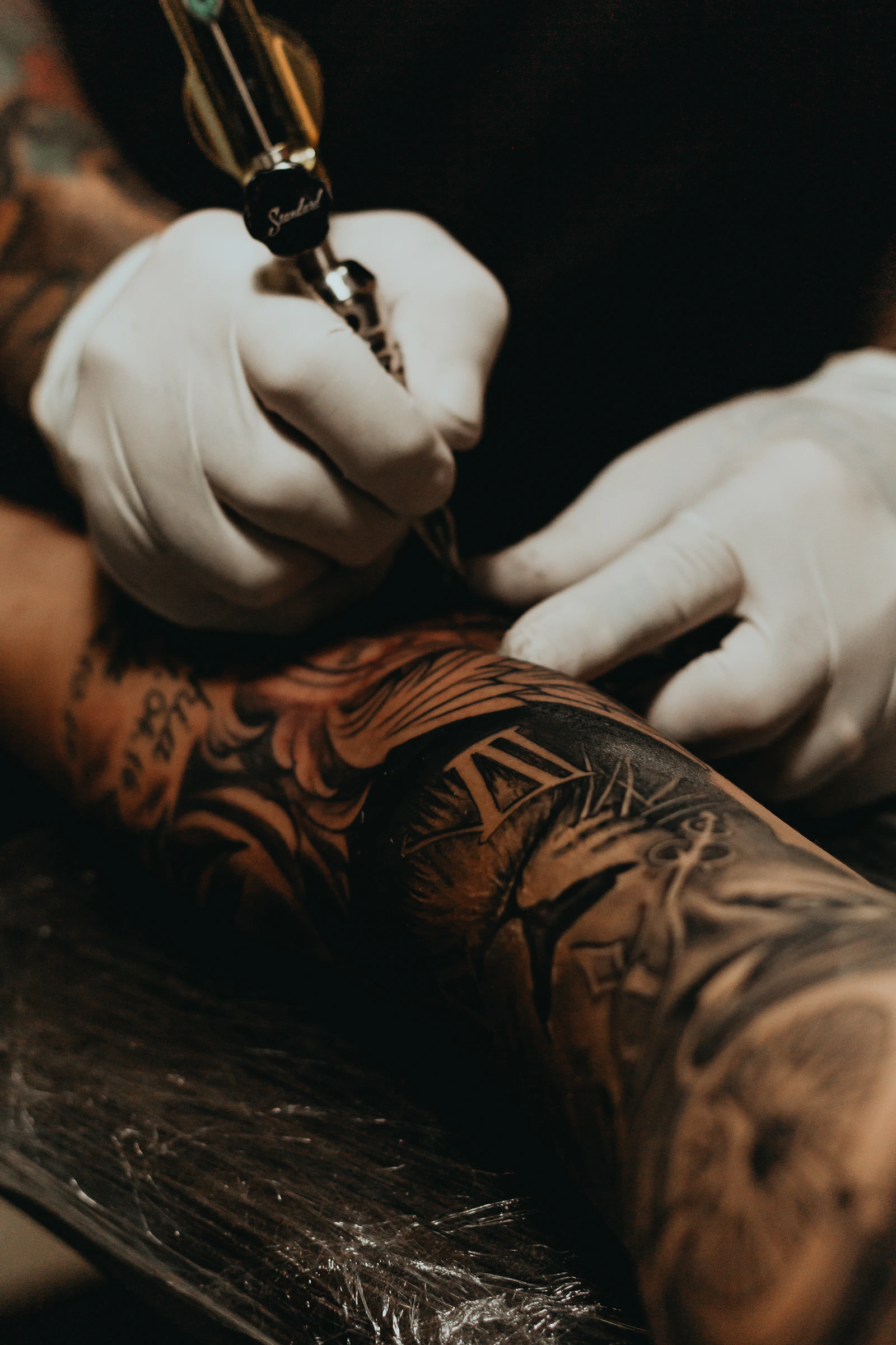 Dark moody portrait of a tattooed forearm resting on a black linen-draped bench.