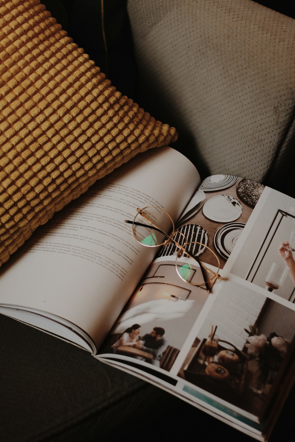 eyeglasses on magazine beside throw pillow on sofa