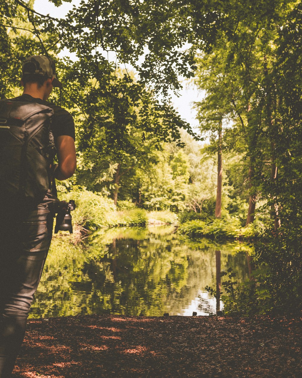 man standing near body of water surrounded by trees