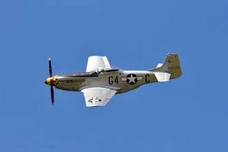 A vintage World War II fighter plane soaring above a battlefield at dawn.