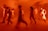 Blurred figures appear to be moving dynamically in a warm, orange-lit space. The image conveys motion and energy with the figures' movements being captured in a state of motion blur.