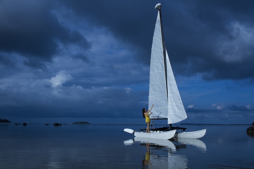 Mulher em pé no barco de vela branco no mar azul durante a noite