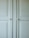 A close-up of a light-colored cabinet door featuring raised panels and two round white knobs. The cabinet's surface has a smooth finish with slight shadows highlighting the contours of the panels.