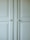 A close-up of a light-colored cabinet door featuring raised panels and two round white knobs. The cabinet's surface has a smooth finish with slight shadows highlighting the contours of the panels.