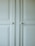 A close-up of a light-colored cabinet door featuring raised panels and two round white knobs. The cabinet's surface has a smooth finish with slight shadows highlighting the contours of the panels.