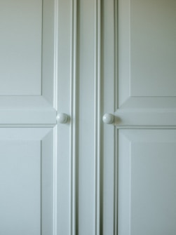 A close-up of a light-colored cabinet door featuring raised panels and two round white knobs. The cabinet's surface has a smooth finish with slight shadows highlighting the contours of the panels.
