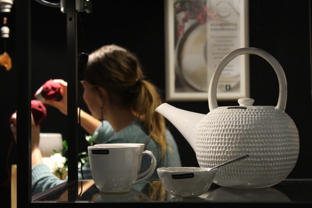 a woman sitting at a table with a tea pot and cup