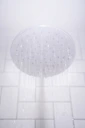 Close-up of a shiny showerhead spraying water in a tiled bathroom.