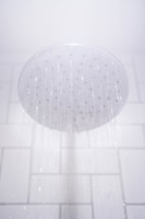 A showerhead releasing streams of water against a white tiled bathroom wall.