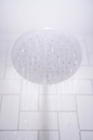 Hands of a plumber installing a modern showerhead against a tiled bathroom wall.