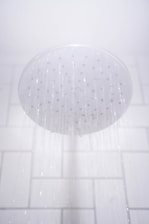 A showerhead releasing streams of water against a white tiled bathroom wall.