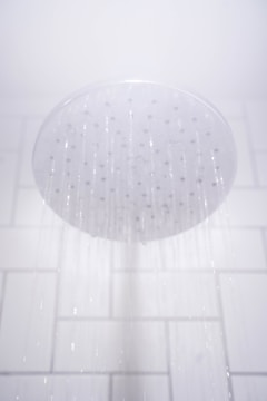 A showerhead releasing streams of water against a white tiled bathroom wall.