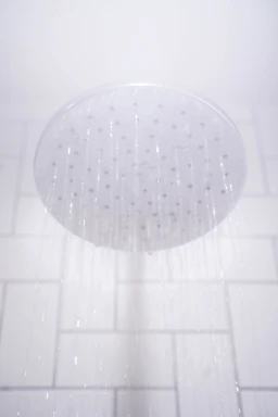 A showerhead releasing streams of water against a white tiled bathroom wall.