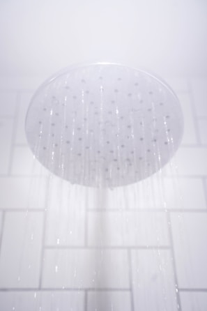 A showerhead releasing streams of water against a white tiled bathroom wall.