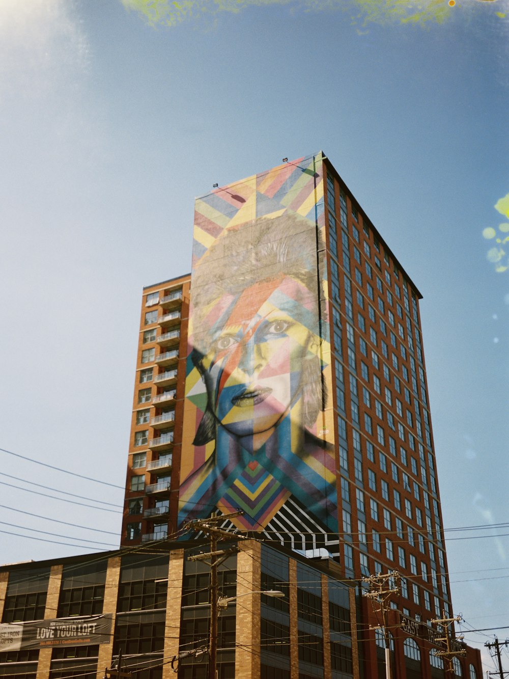 Edificio marrón de gran altura con pintura gráfica multicolor de la mujer bajo cielos azules y blancos durante el día