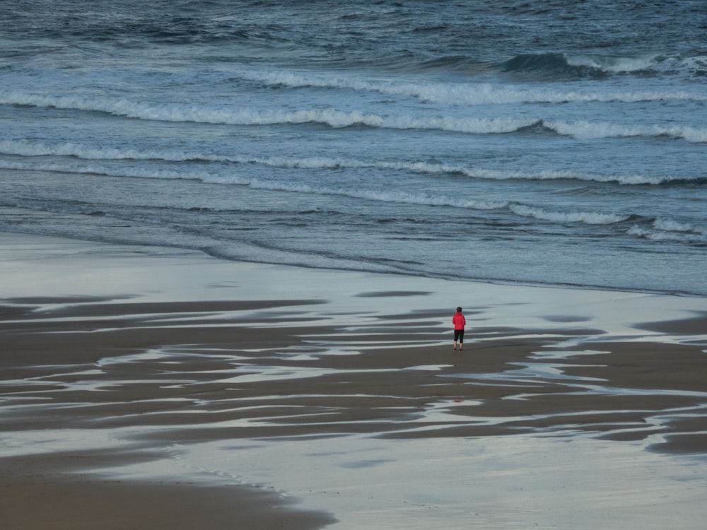 Person mit rotem Hemd steht am Meeresufer