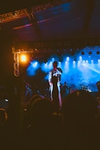 An artist performing on stage with dynamic lighting in a lively event setting.
