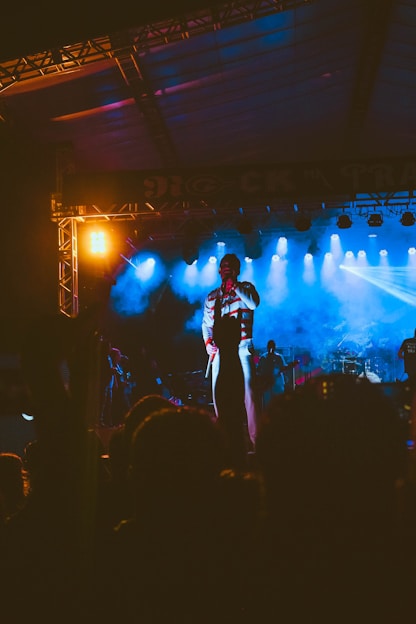 A vibrant photo of Joni Zwick performing stand-up comedy on stage with royal blue and orange lighting.