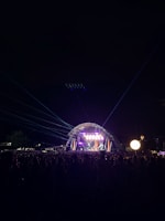 An outdoor concert stage lit with golden lights against a dark night sky.