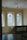 A serene interior space featuring large windows with colorful stained glass panels. The walls are a neutral color, and the room is softly lit by pendant lights hanging from the ceiling. A classical marble bust is placed on a pedestal at the bottom of a staircase with ornate railings.