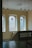 A serene interior space featuring large windows with colorful stained glass panels. The walls are a neutral color, and the room is softly lit by pendant lights hanging from the ceiling. A classical marble bust is placed on a pedestal at the bottom of a staircase with ornate railings.