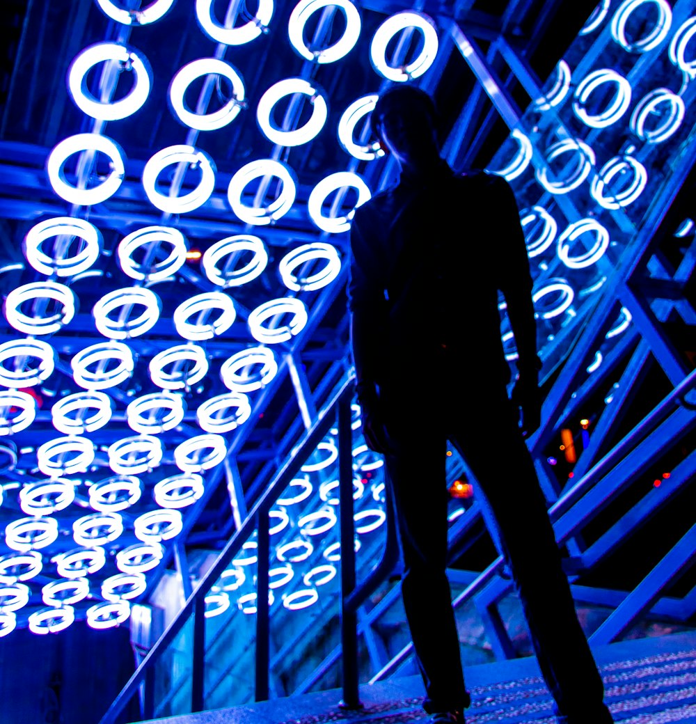 man standing near handrail under neon lights