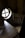There is a rustic wooden chair next to a small wooden table. The table has a cloth partially on it, and both pieces of furniture have a distinct natural wood grain. A round window with a cross design is seen on the left side, allowing some light into the otherwise dark room.