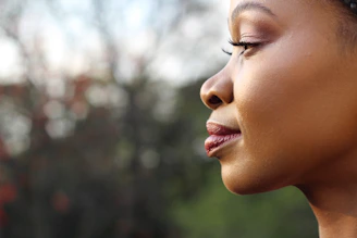 Softly lit close-up of a smiling woman gently touching her glowing, fresh face against a cream background