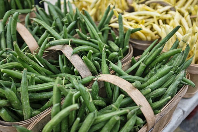 Baskets filled with fresh green beans and yellow wax beans are arranged in close proximity. The beans are vibrant, displaying their freshness, and the baskets have rustic wooden handles.
