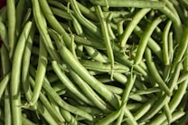 A close-up of a pile of fresh green beans, showcasing their smooth texture and vibrant green color. The beans are arranged in an overlapping manner, highlighting their elongated shape and healthy appearance.