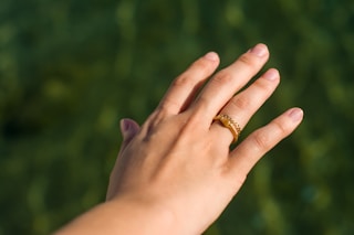 person's hand wearing gold-colored ring