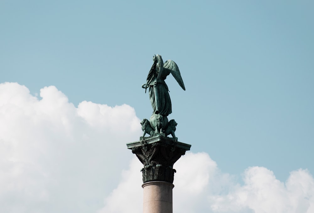 statua alata grigia attraverso il cielo blu e le nuvole