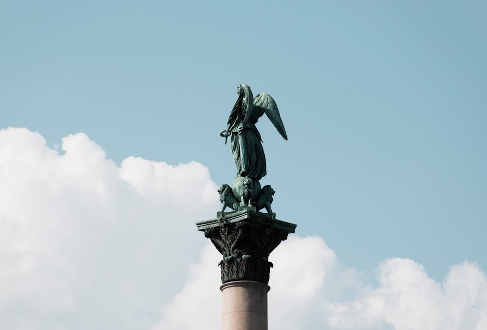 gray winged statue across blue sky and clouds