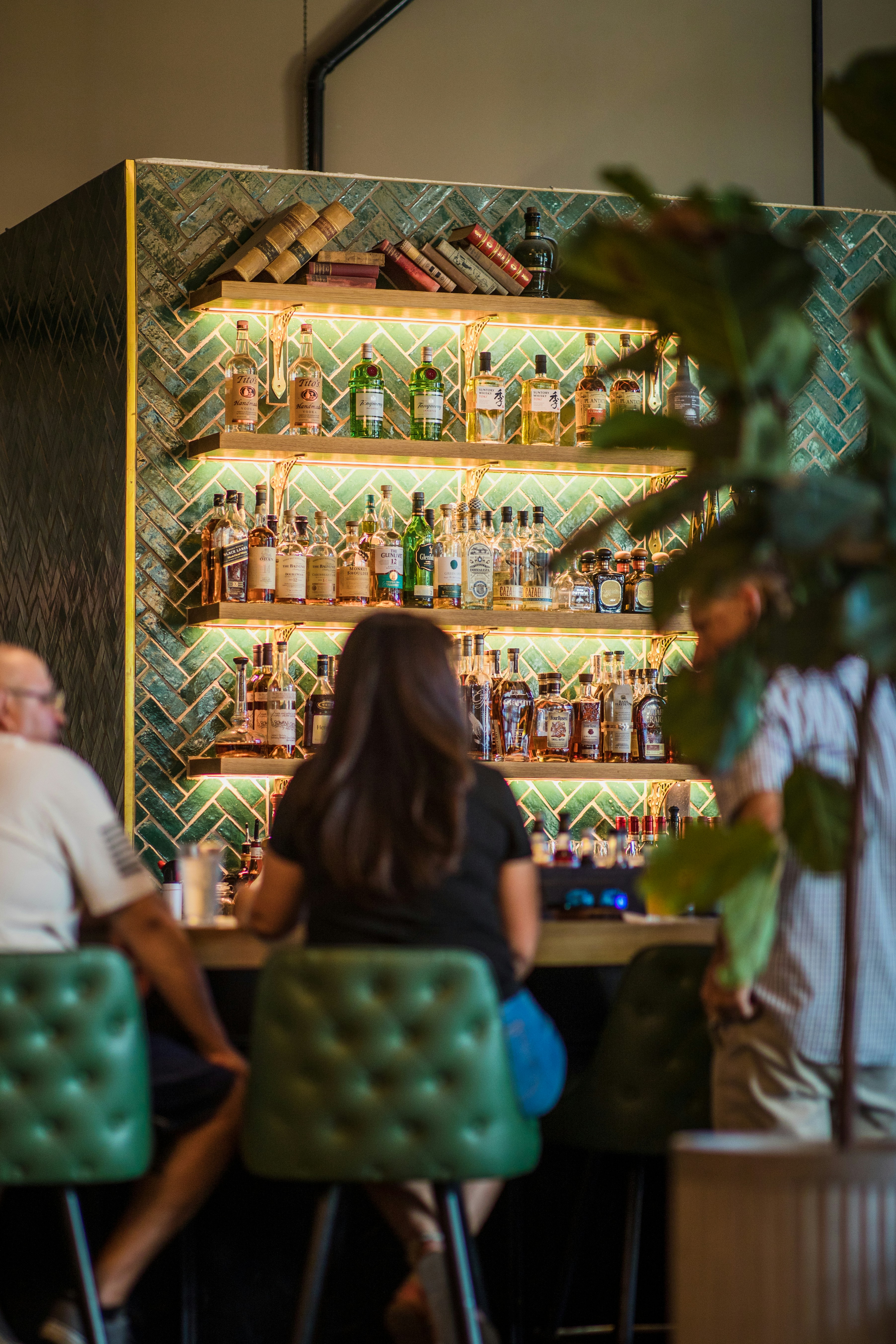 woman wearing black crew-neck shirt and blue jeans sitting on green tufted barstool