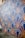 A wall mural features an intricate geometric pattern with fan-like shapes outlined in gold against a dark blue background. The design includes stylized green vine elements that add a touch of nature. The mural extends along a street, providing an eye-catching artistic presence.