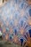 A wall mural features an intricate geometric pattern with fan-like shapes outlined in gold against a dark blue background. The design includes stylized green vine elements that add a touch of nature. The mural extends along a street, providing an eye-catching artistic presence.