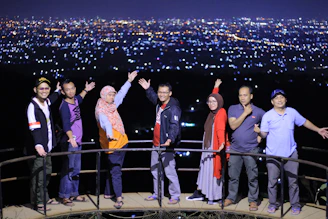 A vibrant group photo of seven stylish travelers posing in front of Tokyo Tower at sunset, their summer outfits bright and full of personality.