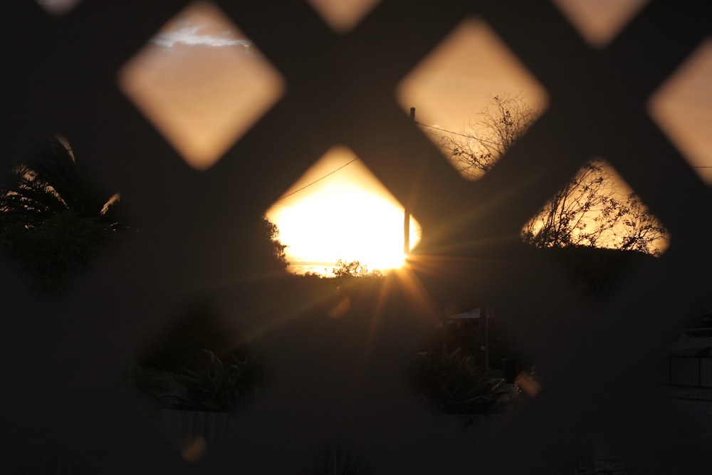 the sun is setting through a latticed fence
