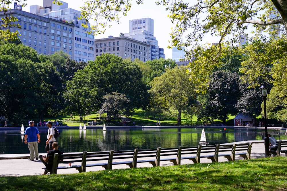 two walking people between empty benches and body of water during daytime