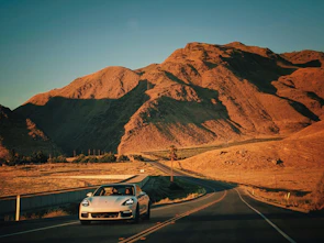 Porsche Macan cruising along a desert highway with red rocks in the background.